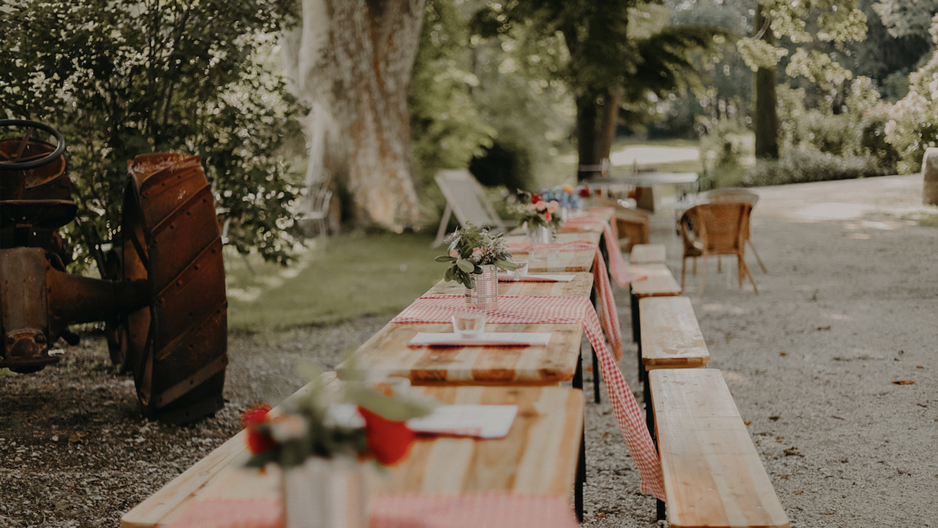 Prise de vue simple d'une table en bois décorée style picnic chic, avec des nappes vichy et des fleurs rouges et blanches pour un style garden party chic