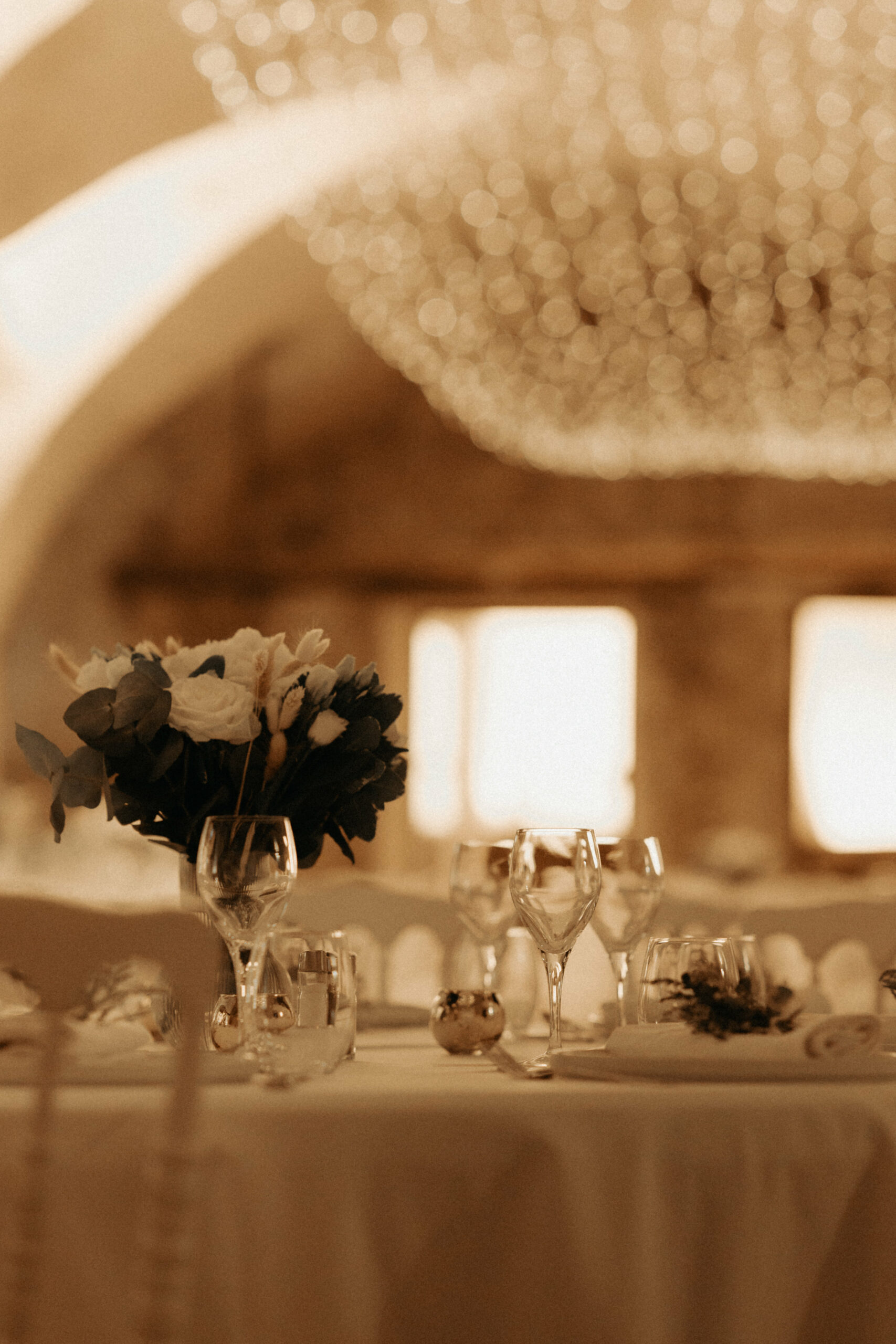 prise de vue de la salle en mise au point large et grand flou, mettant en valeur la table des marié, tout en blanc et le bouquet de roses blaches qui y trône en plein centre