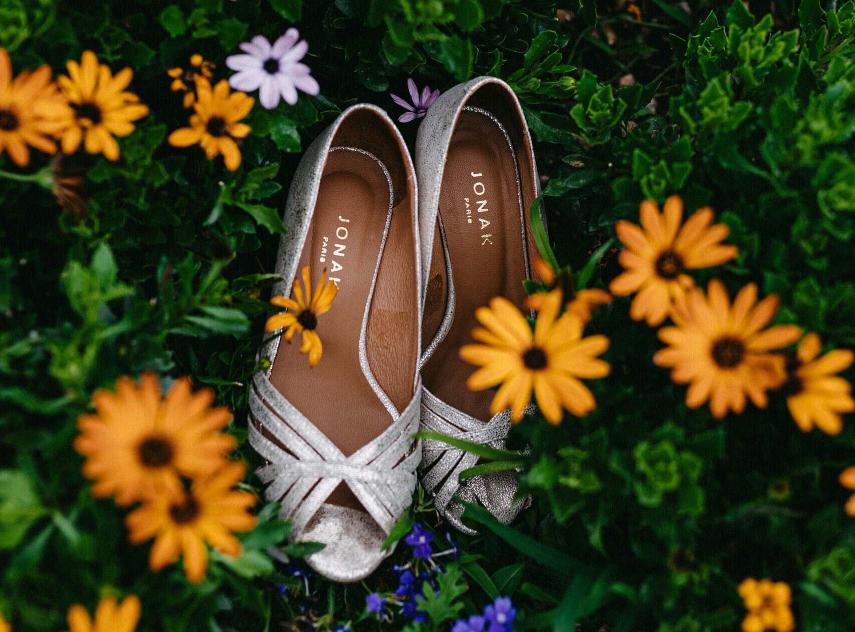 Plan resserré sur les chaussures de la mariée posées dans les fleurs d'un jardun coloré