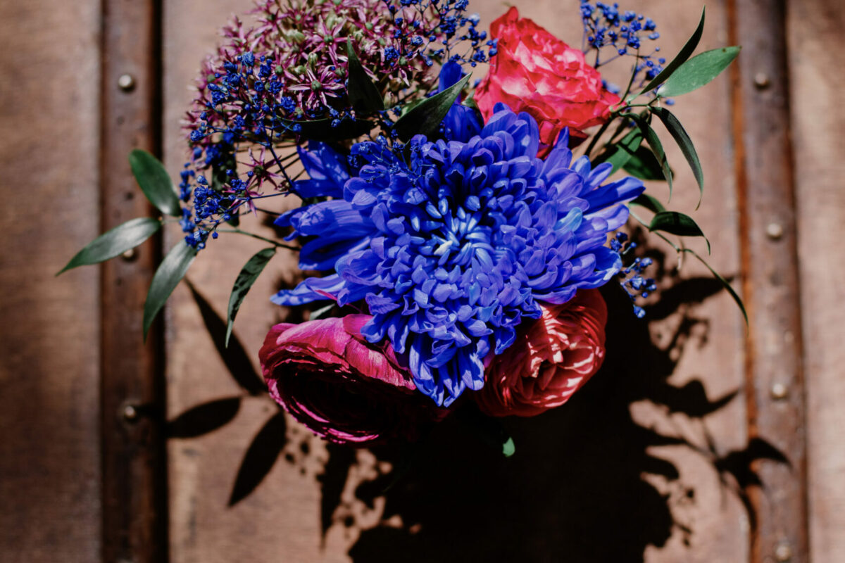 vue de haut sur un bouquet rouge et bleu, posé sur une valise vintage en cuir marroné et polie par le temps